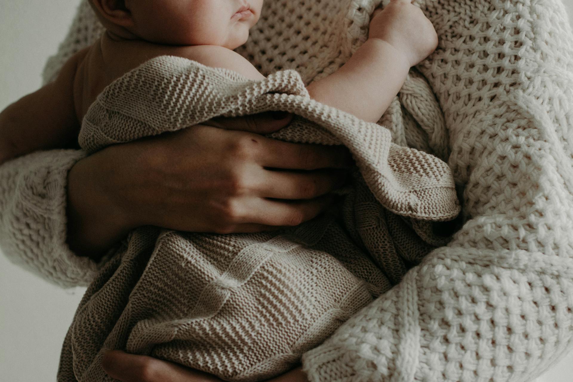 Person holding a baby wrapped in a beige knitted blanket